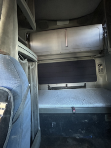 Cargo area of an old Freightliner FC2 sleeper cab showing side storage box, interior steps, and fabric seat in view.