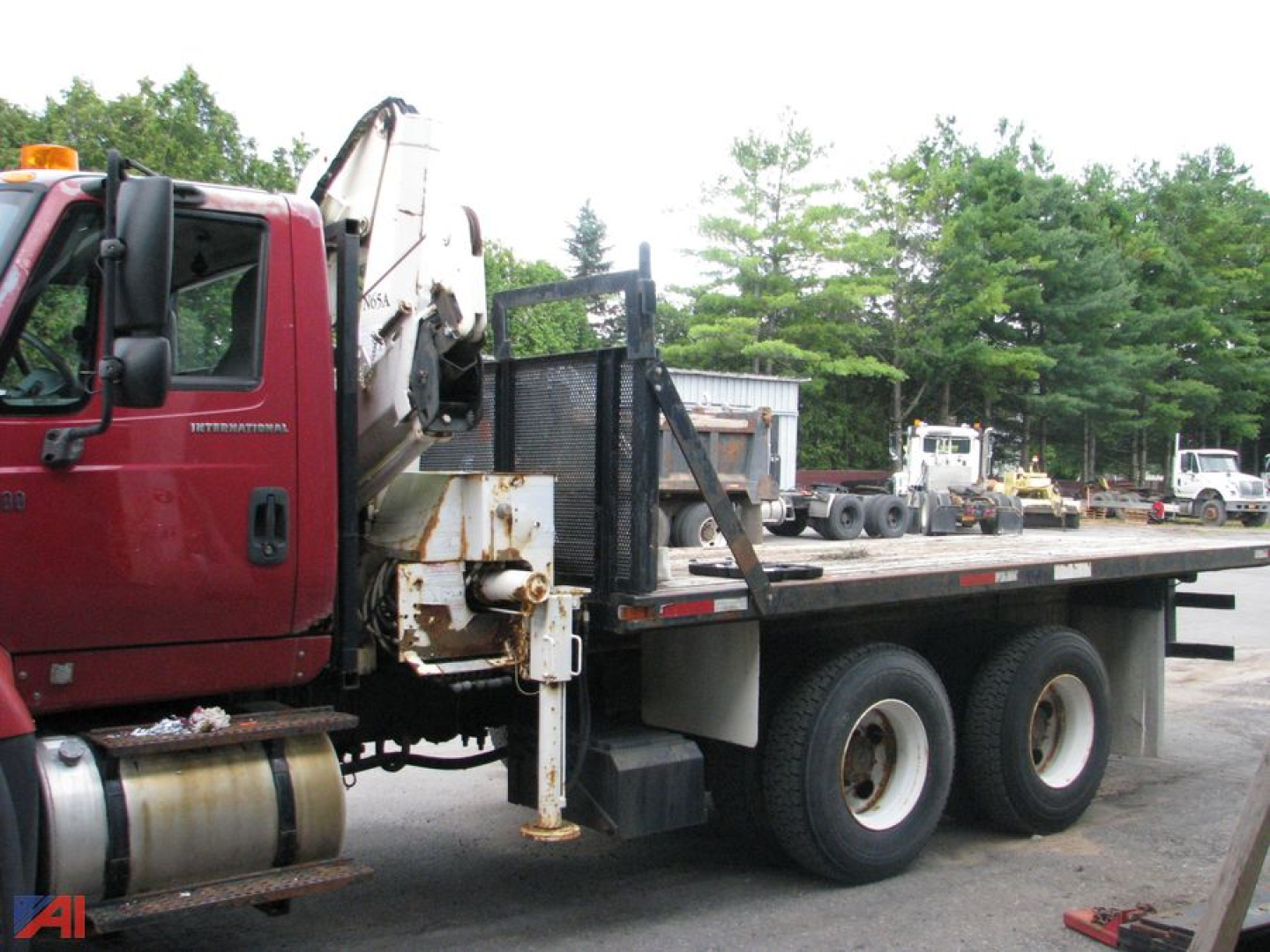Flatbed truck with a mounted crane on the cab and a long flatbed, International SF547 WorkStar style, showing dual rear wheels and a parked equipment yard.