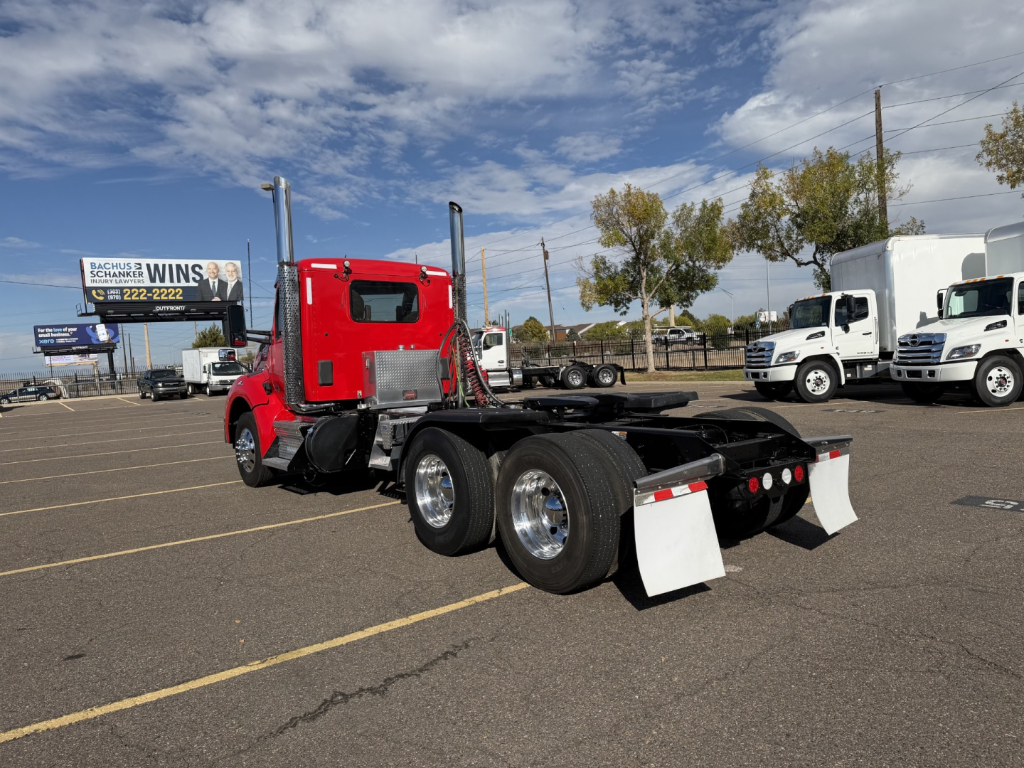 Kenworth T880 conventional daycab truck in a lot, red cab, black chassis, dual rear axles, white mud flaps, no trailer attached, clear blue sky.