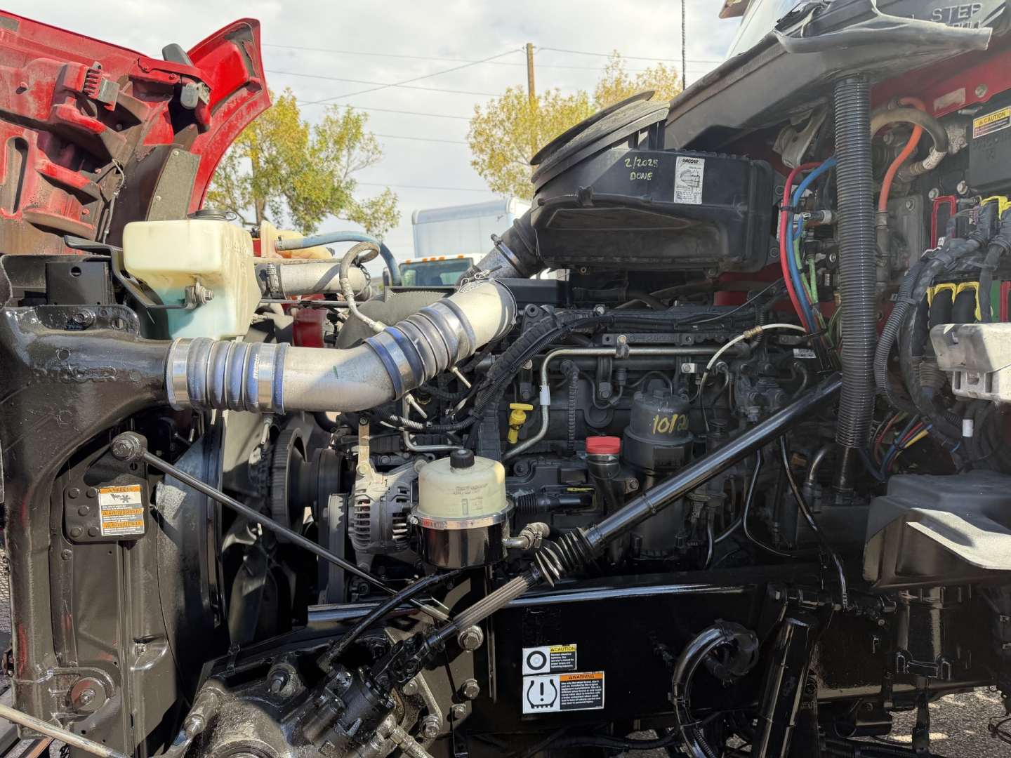 Kenworth T880 truck engine bay with exposed components, hoses, and wiring; visible labels and reservoirs in an in-service configuration.