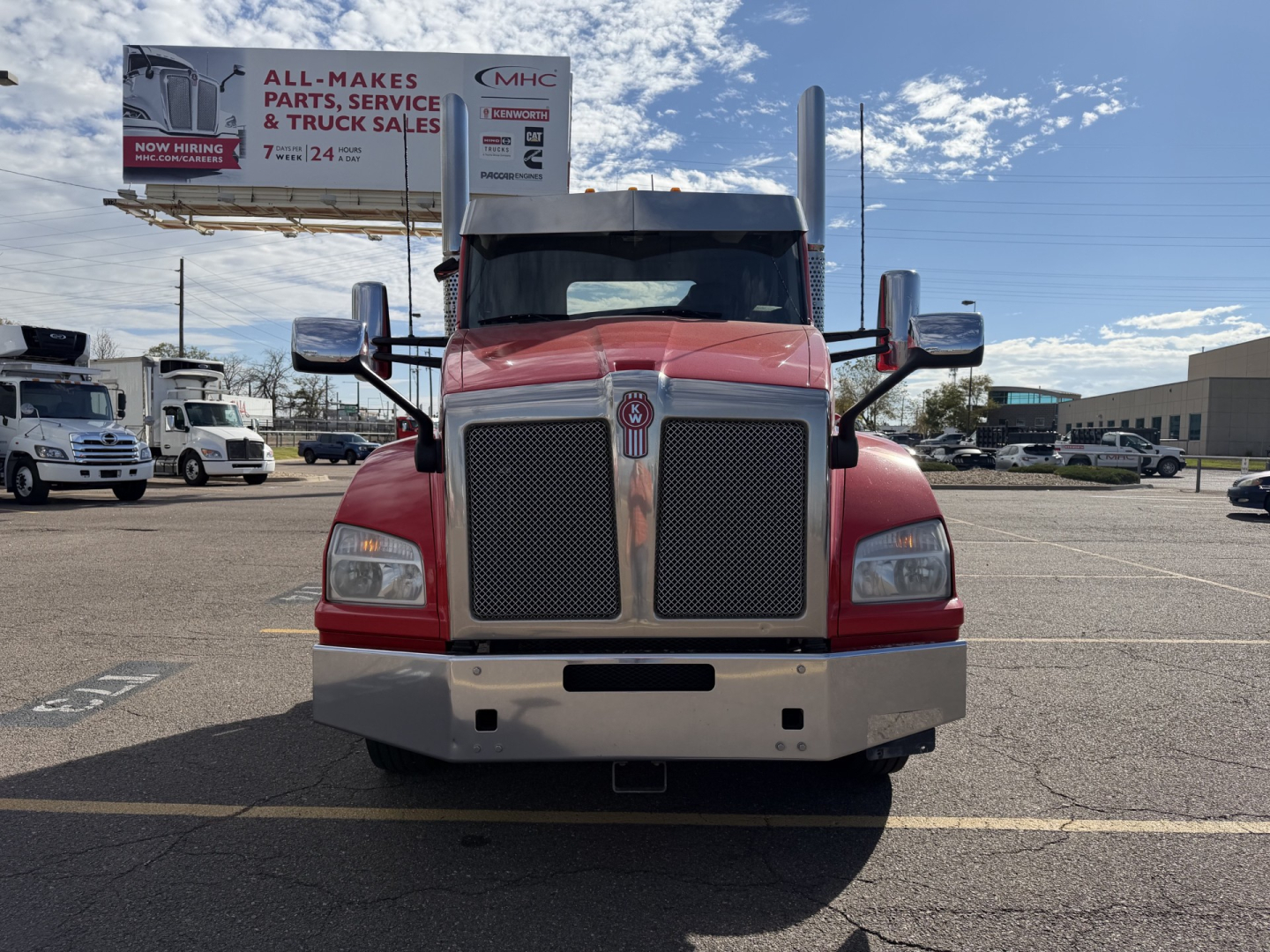 Kenworth T880 conventional daycab front view showing large chrome grille, dual tall exhaust stacks, red cab with gray bumper.