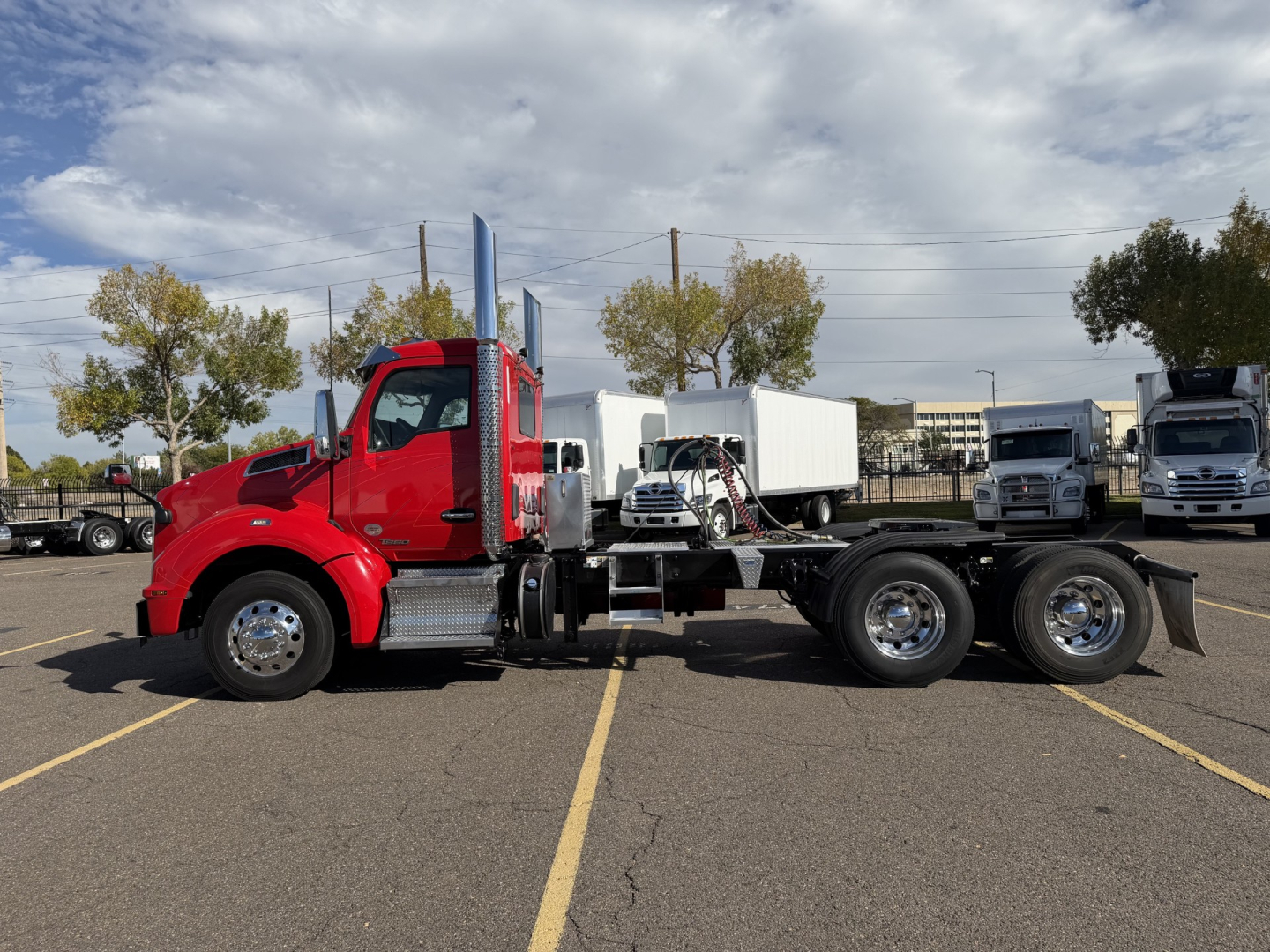 Kenworth T880 truck chassis side view showing red cab and dual rear axles with grasshopper exhaust stack and white cargo trailer in background.