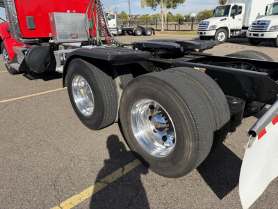Kenworth T880 truck chassis showing dual rear wheels and aluminum rims with black frame; red cab in background; tires and fifth wheel area visible.