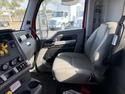 Kenworth T880 truck interior view showing front seat and dashboard with steering wheel, controls, and window; outside shows other trucks in lot.