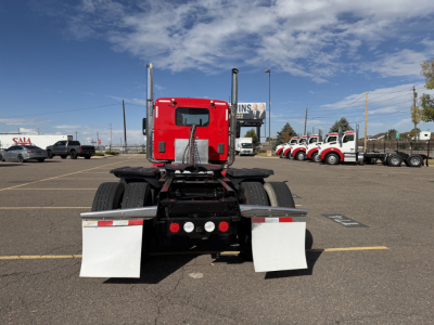 Rear view of a red Kenworth T880 daycab tractor in a parking lot showing mud flaps and chassis with dual rear axles.