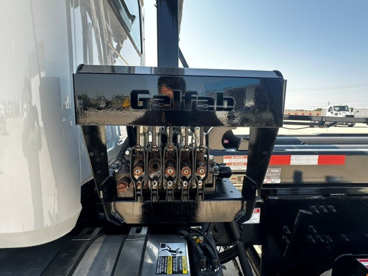 Front view of a new Mack GR64B roll-off truck showing hydraulic hose manifold and 'Galfab' label on the black component