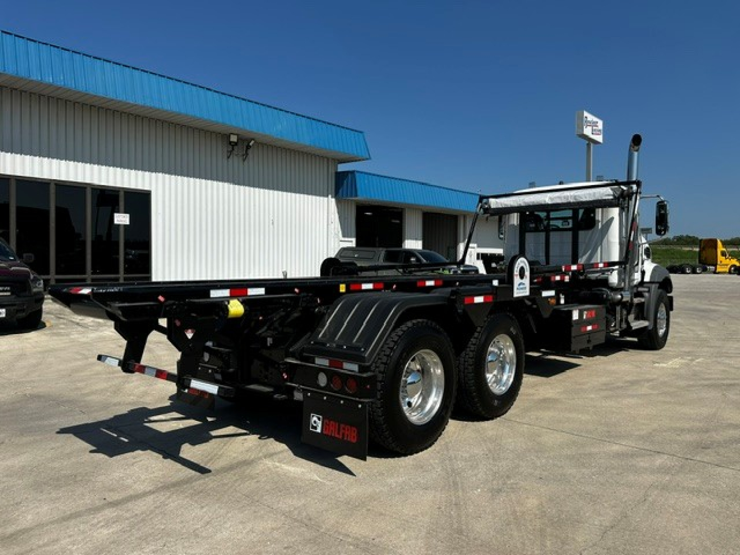 New Mack GR64B roll-off truck showing chassis, tandem rear axles, and empty flatbed with safety rails and mud flaps.