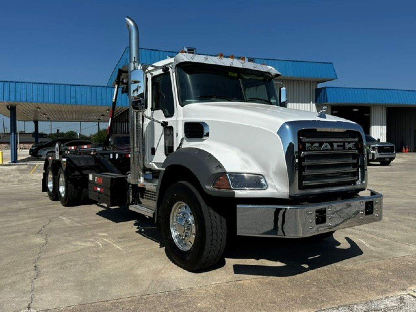 Truck in a lot showing a 2027 Mack GR64B roll-off chassis with chrome front bumper and black grille, VIN 1M2GR2GC2VM058607, stock 73195.