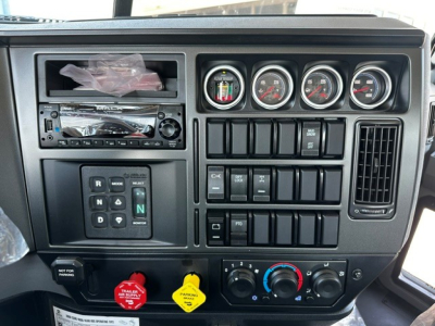 Dashboard of a 2027 Mack GR64B rolloff truck showing steering wheel area with analog gauges, radio, various switches, and climate controls.