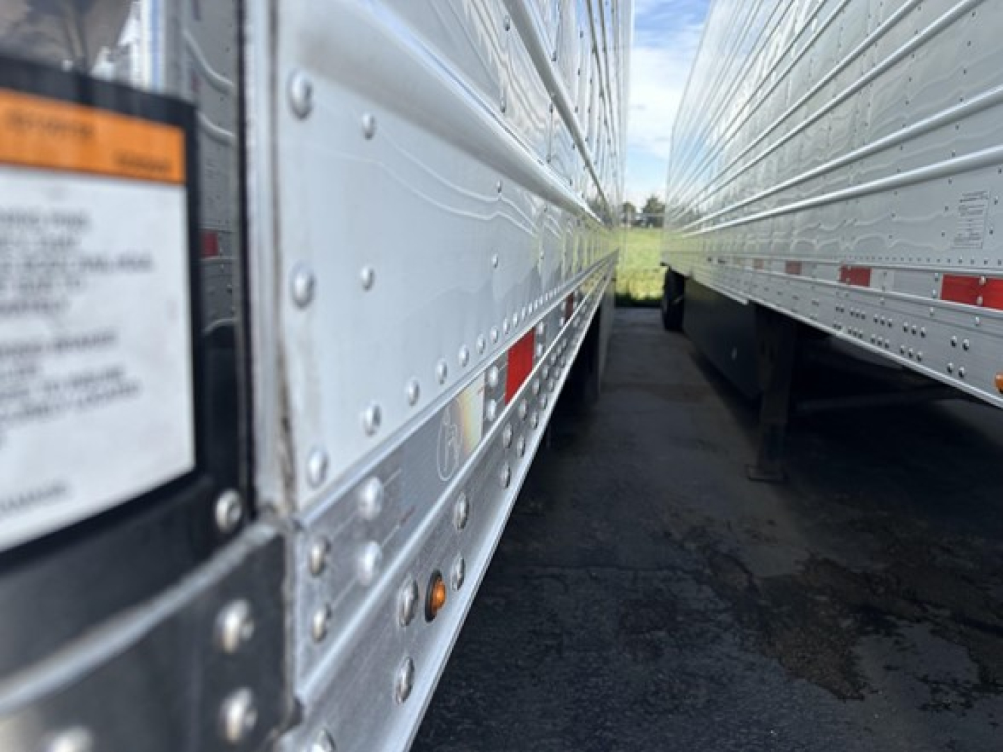Side view of a 2023 Great Dane Carrier trailer, metal siderails with rivets, similar trailers in a row, narrow alley between them.