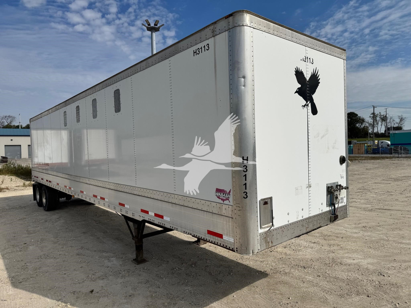 Trailer side and rear of a 2014 Wabash chip trailer showing white exterior, vent windows, bird decals, and rear access door.
