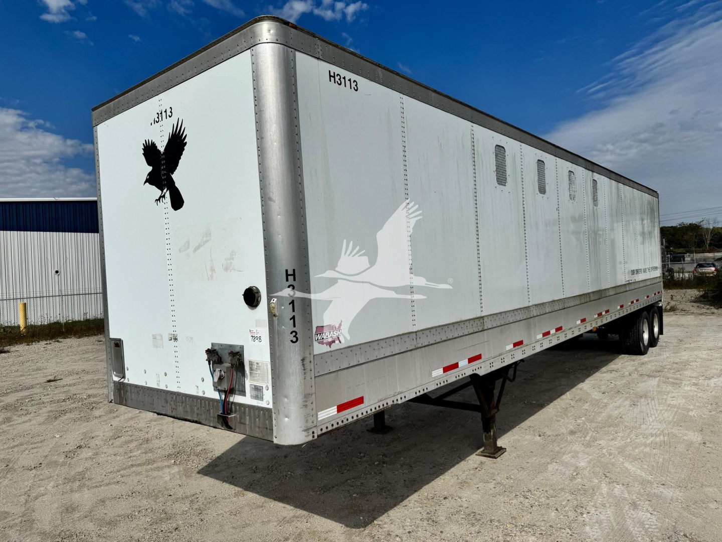 Trailer side view showing long white chip trailer with small windows, black eagle graphic on rear, and registration numbers H313 on door, H3113 on top edge.