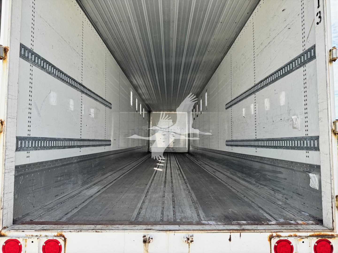 Trailer interior showing empty cargo bay with metal side walls and ribbed floor, white exterior with rear lights visible.