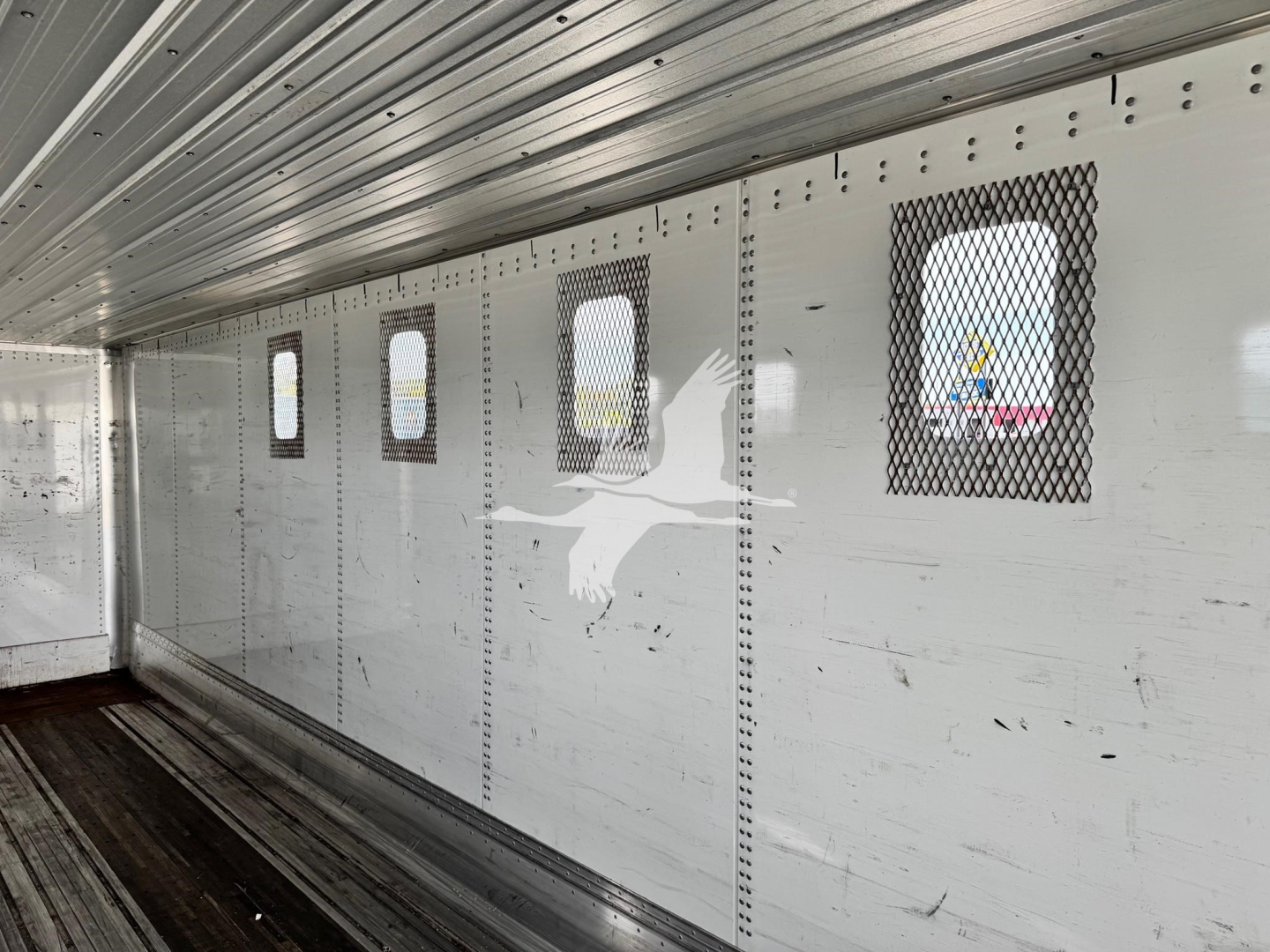 Trailer interior wall with small rectangular windows and vents, metal riveted panels, chip trailer style cargo area.