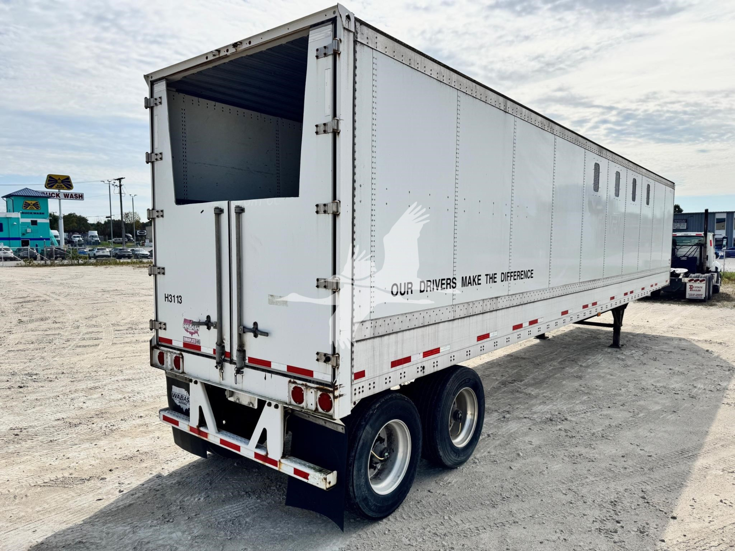 Trailer showing white Wabash chip trailer with dual rear doors, open hopper at back, stamped identifiers, and safety decals on side.