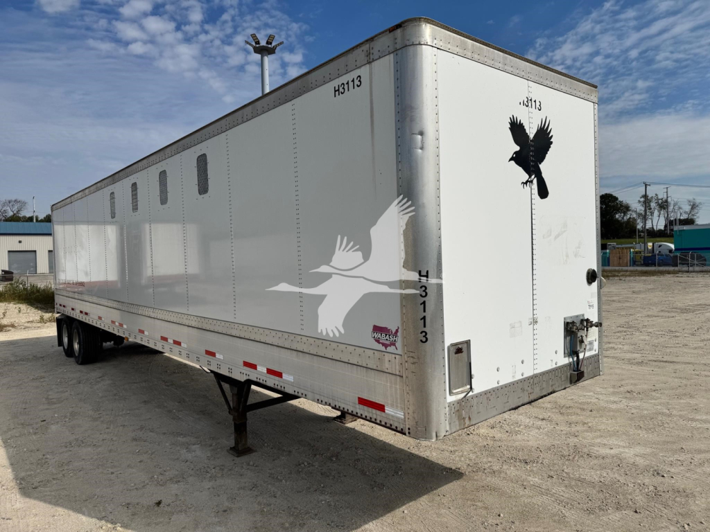 Trailer side and rear of a 2014 Wabash chip trailer showing white exterior, vent windows, bird decals, and rear access door.