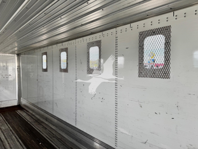 Trailer interior wall with small rectangular windows and vents, metal riveted panels, chip trailer style cargo area.