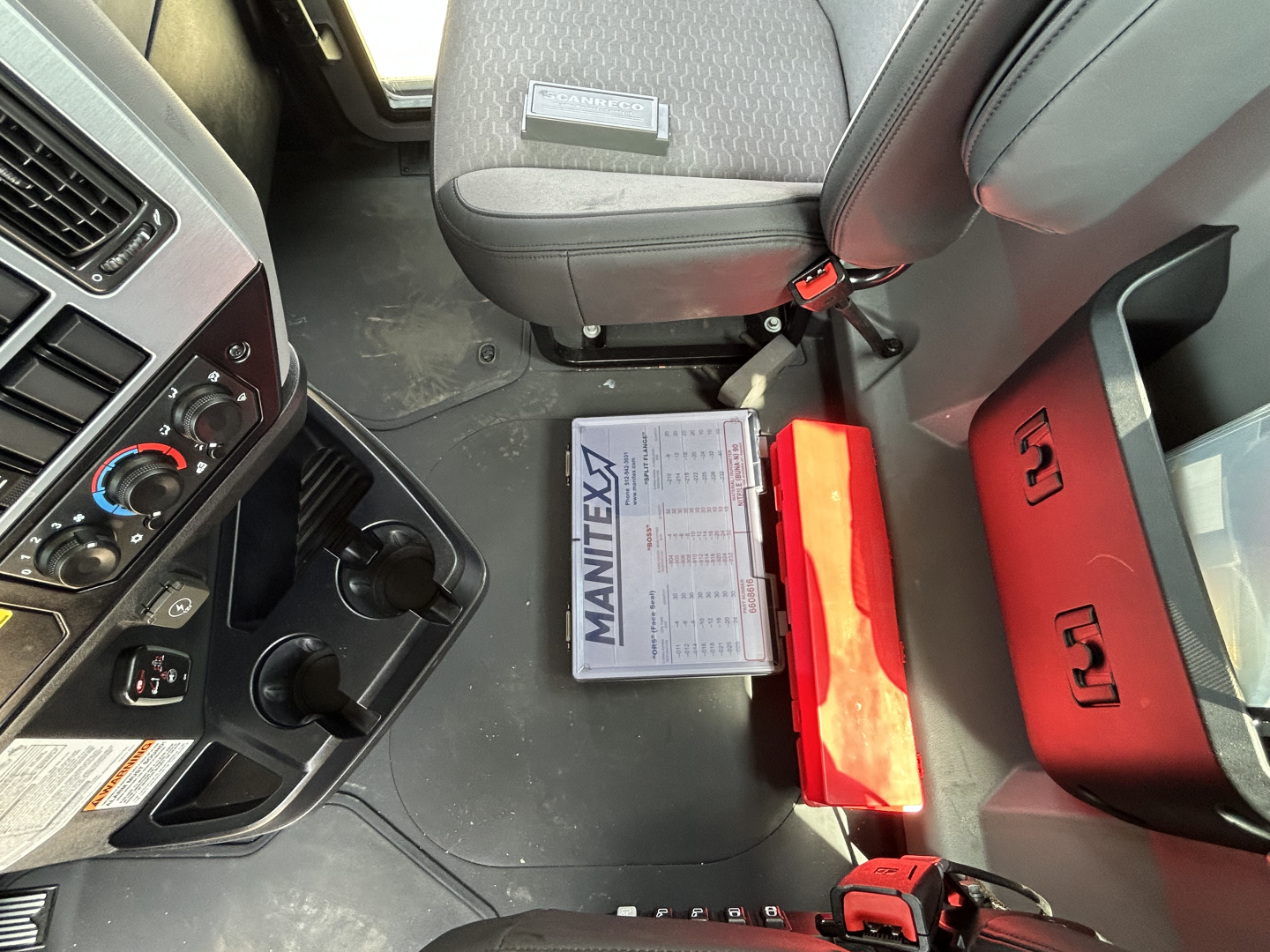 Mack GR64F truck cab interior showing dashboard controls, steering column, and MANITEX label on documents in footwell.