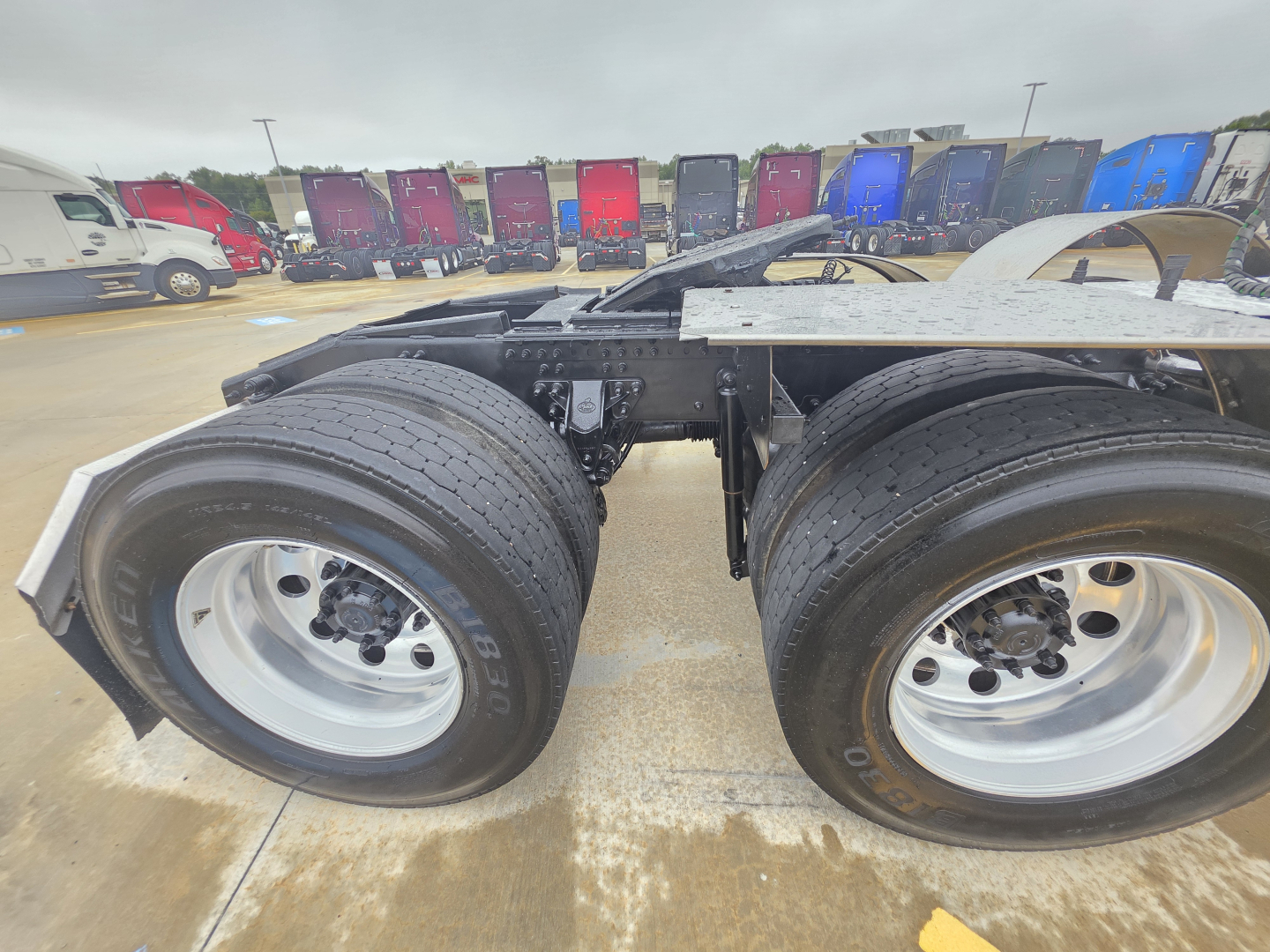 Mack Pinnacle 64T truck chassis view with dual rear axles and large tires. In the background are multiple colored trailers.