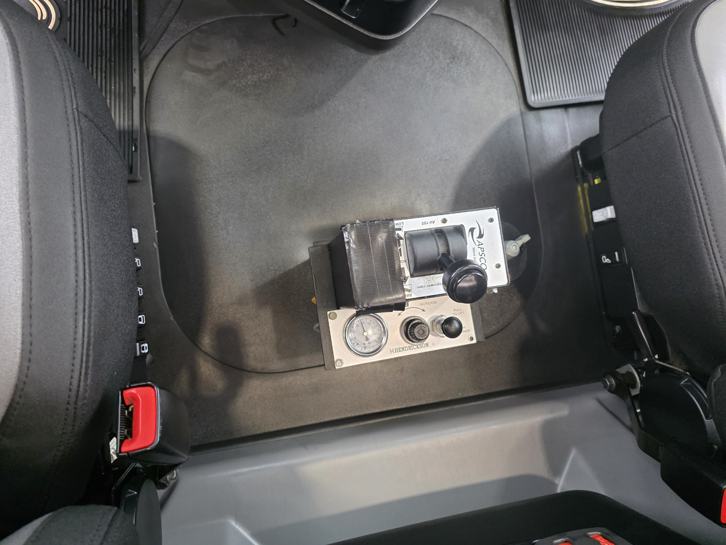 Cab interior floor area with control module and two seat bases visible between the seats.