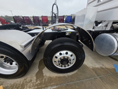 Wheel well and front axle of a Mack Pinnacle 64T truck showing the front tire and wheel, with fender and part of the cab/frame; no legible text visible on components.