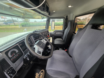 Cab interior of a 2020 Mack Pinnacle 64T shown from the driver’s side, steering wheel, dashboard gauges, and two front seats visible.