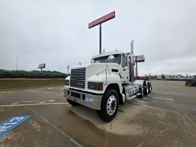 Truck: 2020 Mack Pinnacle 64T conventional daycab, white exterior, front grille, dual rear axles, fuel tanks, and dealership lot in background.