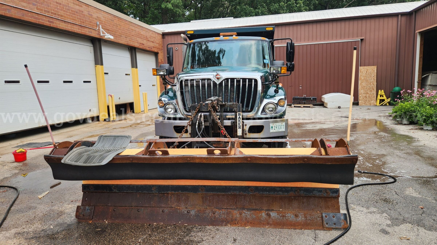 Front view of a 2013 International 7400 plow truck with a large steel snow plow attached. The truck grille, headlights, and a chain winch are visible. VIN label and stock number not legible in image.