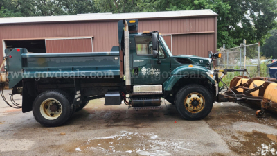 Dump truck with plow attachment in a yard, green cab, dual rear wheels, logo with 'Old Dominion College' (blurry) on door, watermarked govdeals, side view.