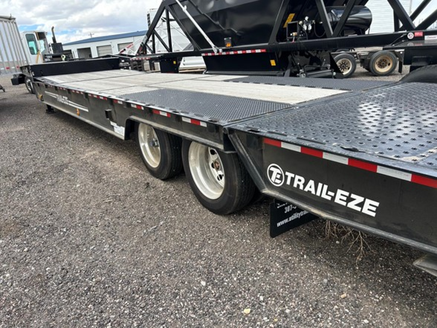 Trailer showing a large flatbed trailer with metal diamond plate decking, dual rear axles, and TRAIL-EZE branding on the side; underside wheel wells and tires visible.