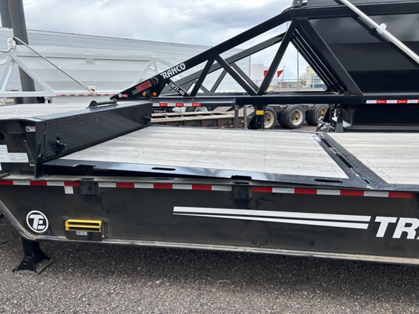 Trail-Eze TE80Ht trailer deck edge and frame with black finish, partial white branding, steel trailer bed, and wheel area visible.
