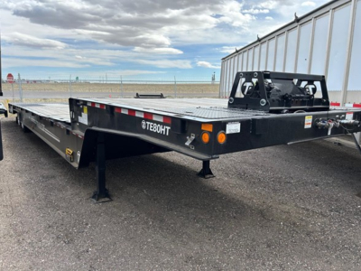 Trail-Eze TE80HT flatbed trailer showing TE80HT branding, front hitch area, black steel frame, orange reflectors, and support legs on a gravel lot.