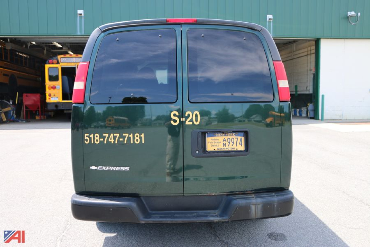 Chevrolet Express passenger van rear view showing S-20 label, contact numbers, and New York vanity plate on dark green metal doors.