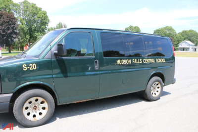 Green Chevrolet Express passenger van with 'HUDSON FALLS CENTRAL SCHOOL' lettering on side and 'S-20' near front wheel.