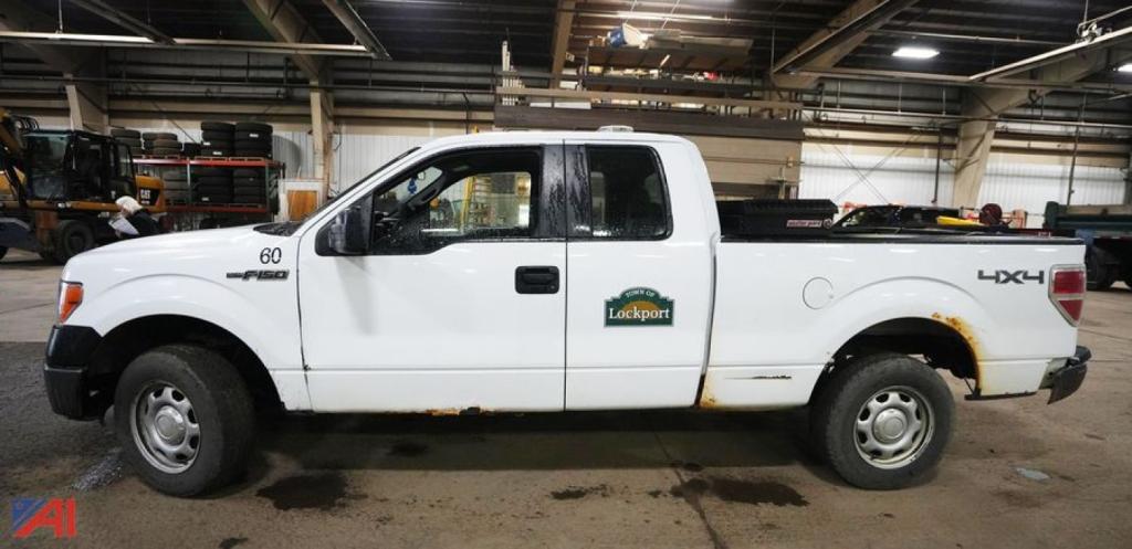 Ford F-150 Extended Cab 4x4 pickup truck in a warehouse setting, white with a tool bed, showing 'Lockport' decal around the door area.