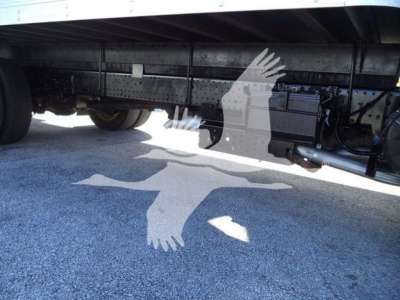 Isuzu NPR HD truck undercarriage showing fuel lines and chassis with a battery box and wiring, side view with gravel ground.