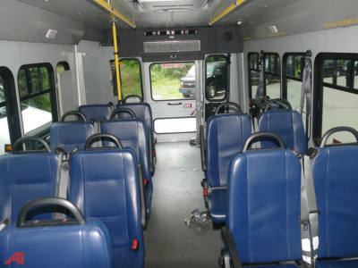 Bus interior with blue seating and wheelchair lift accessible rear area showing multiple rows of seats.