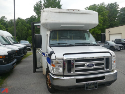 Ford Econoline E450 mini bus front view with wheelchair lift door open on the passenger side, large cargo box overhead, chrome grille, white exterior.