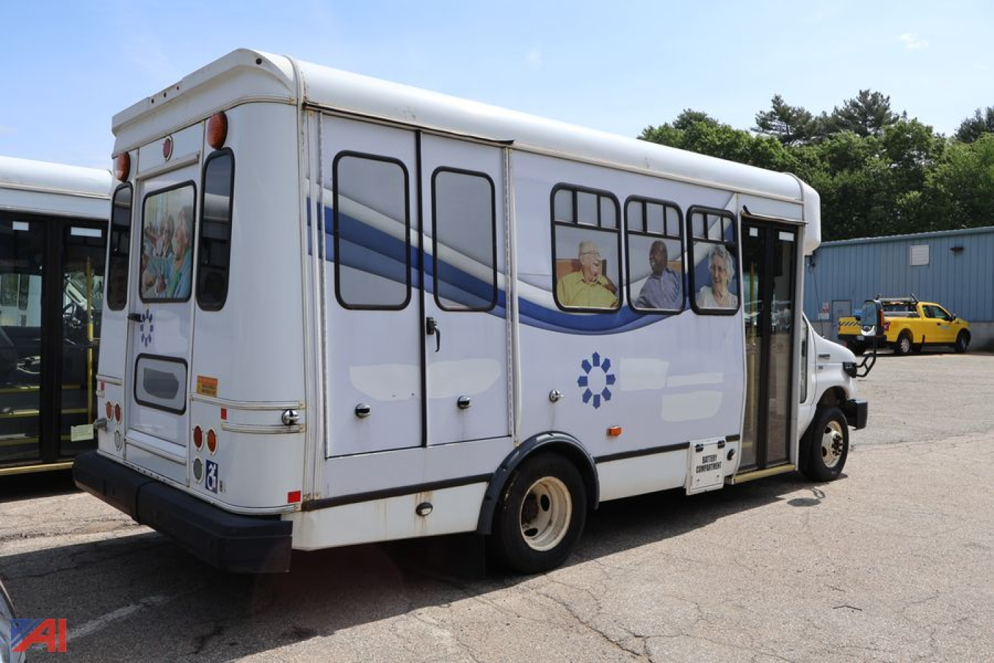 Ford E-350 wheelchair bus rear/right side view showing side windows with blue graphic stripe and wheelchair icons.