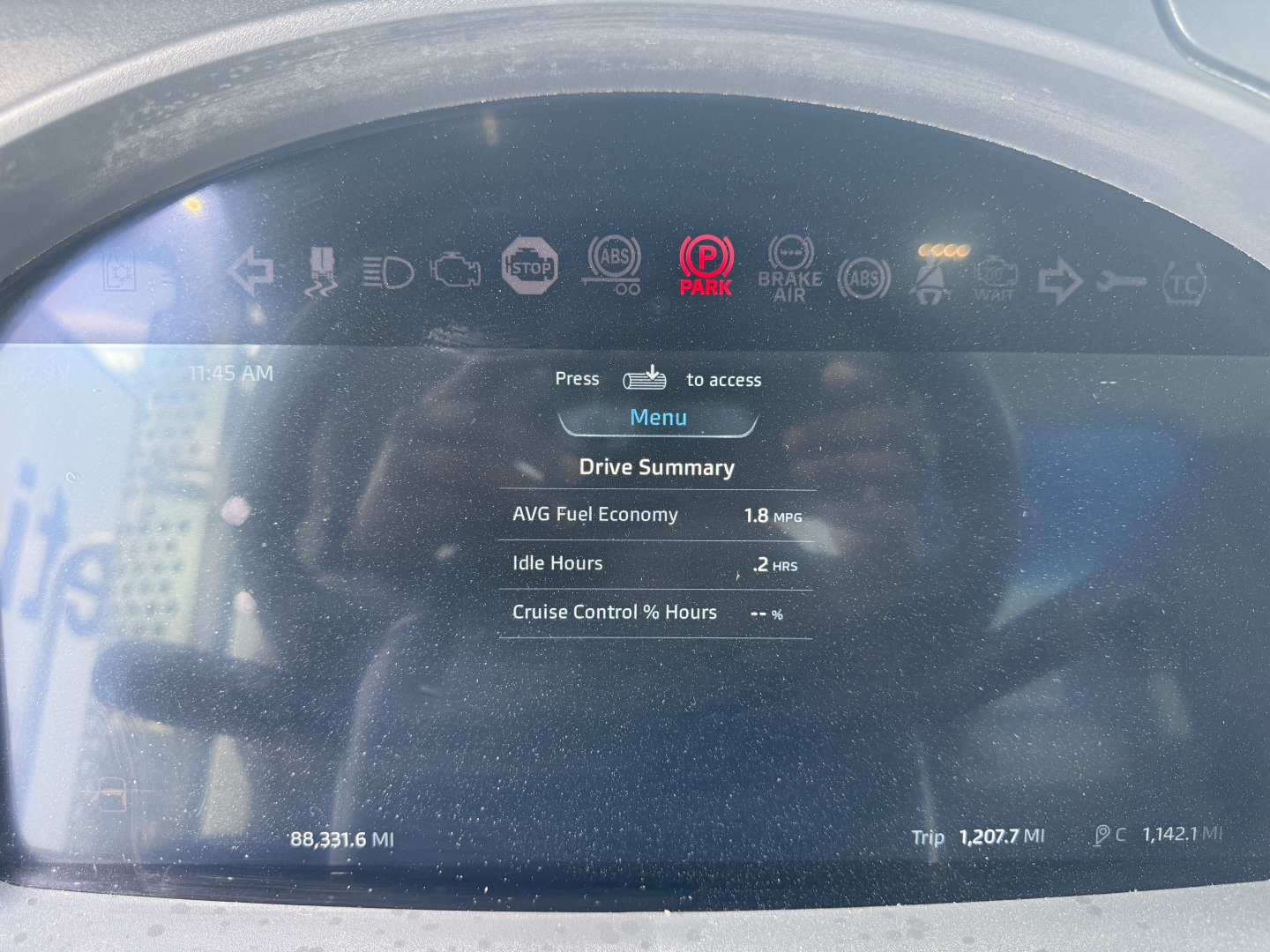 Kenworth T880S instrument panel display showing Drive Summary with AVG Fuel Economy 1.8 MPG, Idle Hours 2. hrs, cruise control hours, and vehicle mileage 88,331.6 MI; trip 1,207.7 MI; P. ID icons at top.
