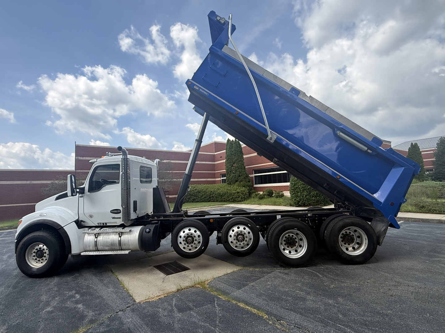 Kenworth T880S dump truck side view showing raised blue dump bed and white cab with multiple axles.