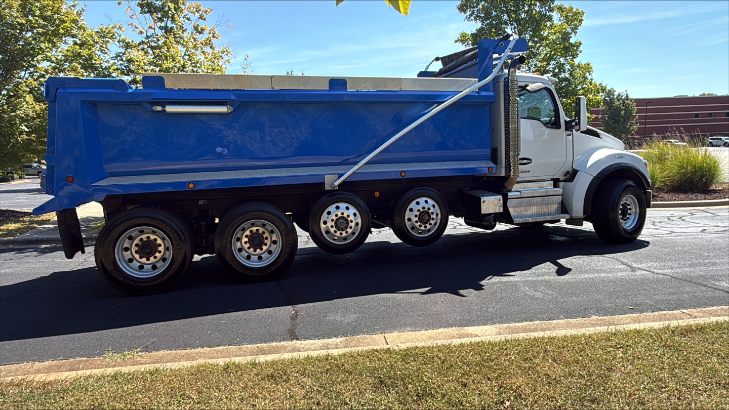 Kenworth T880S dump truck side view showing blue dump bed and white cab with multiple axles.