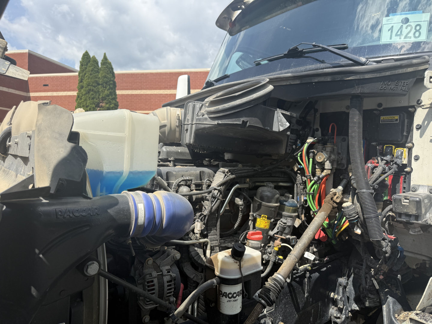 Kenworth T880S engine bay view with hoses, wiring harnesses, and fluids reservoir visible.