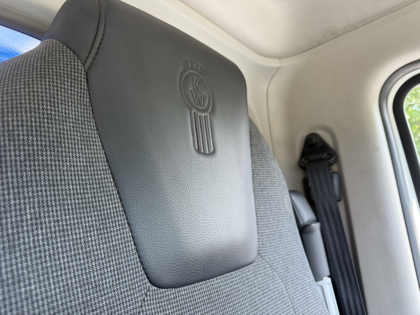 Kenworth logo on seat backrest in truck cabin, with seatbelt and interior panel in view.