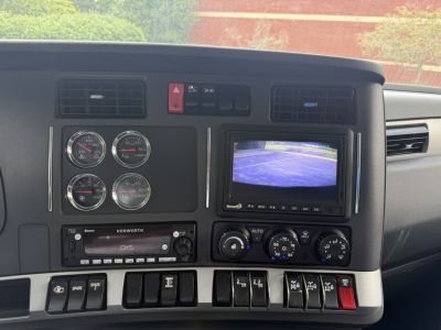 Dash of a 2024 Kenworth T880S dump truck showing gauge cluster, Kenworth radio, climate controls, and a rear-view monitor.