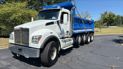 Kenworth T880S dump truck with white cab and blue dump bed, front grille, large tires, and fuel tanks visible.