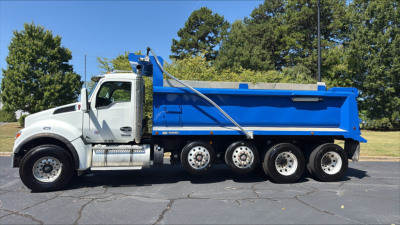 Dump truck showing 2024 Kenworth T880S with blue dump body and white cab, side profile view.