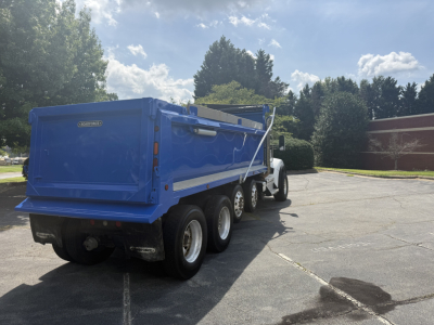 Rear and side view of a blue Kenworth T880S dump truck with a large dump bed and rear tires.