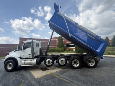 Kenworth T880S dump truck side view showing raised blue dump bed and white cab with multiple axles.