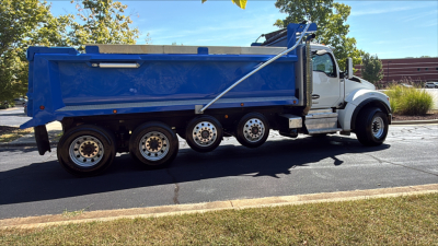 Kenworth T880S dump truck side view showing blue dump bed and white cab with multiple axles.